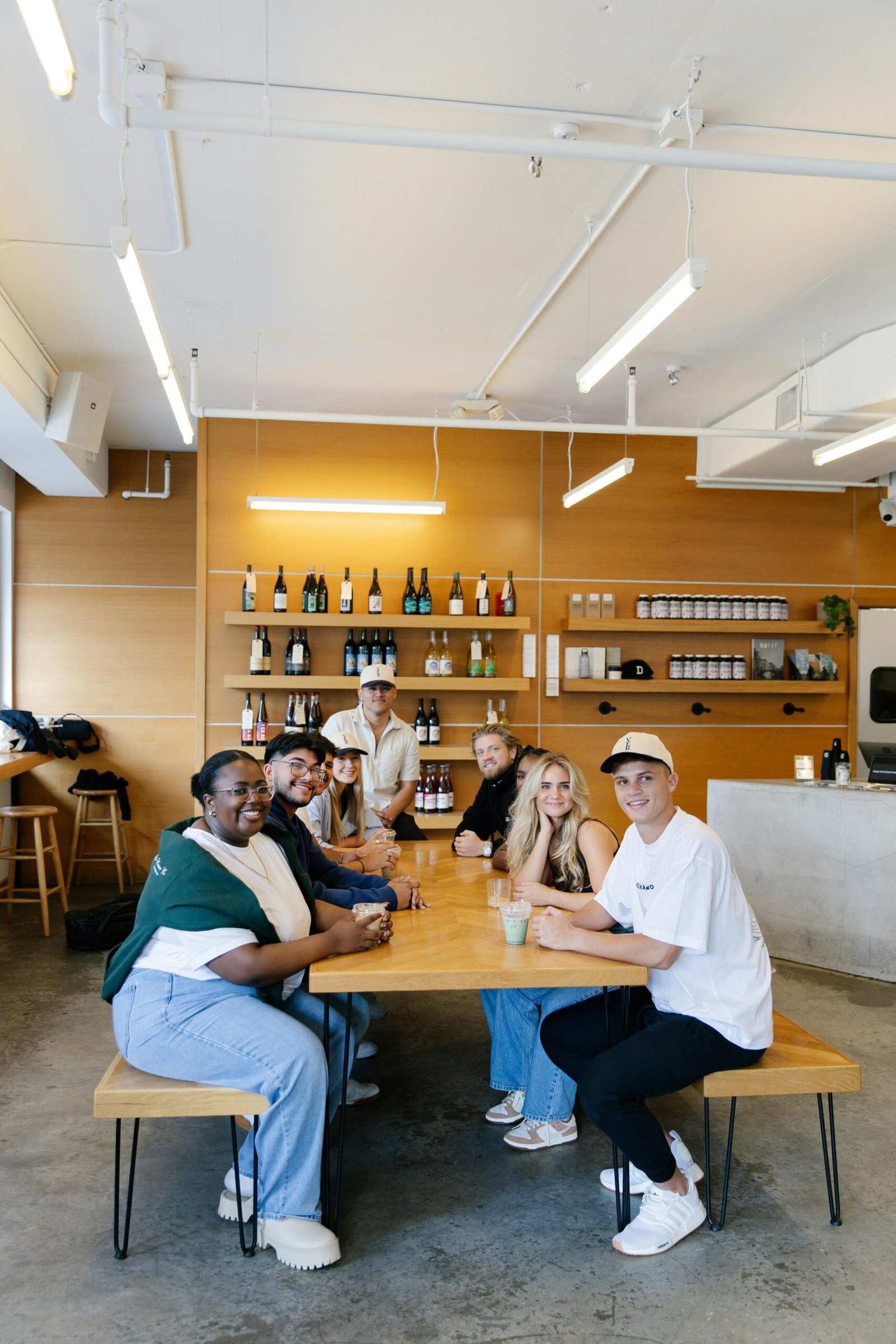 Diverse group of adults socializing at a cafe around a wooden table with a modern interior.